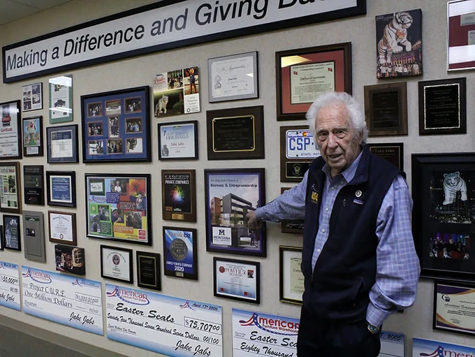 Jake Jabs standing in front of a wall of awards and honors