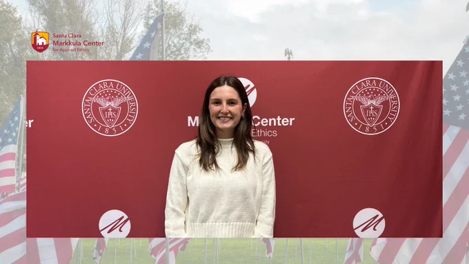 . There is a backdrop with Santa Clara University and the Markkula Center logos, in front of a display of American flags.