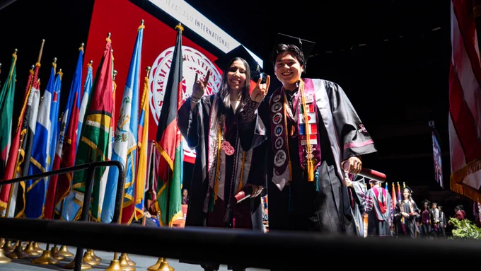 Two Texas A&M International University graduates smiling at the camera and making the "Dust 'Em" hand gesture.