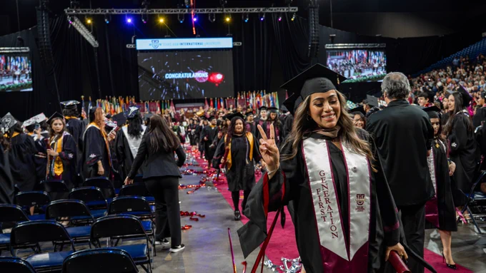 A Texas A&M International University graduate making a peace sign to the camera as they depart from their commencement as a proud graduate.