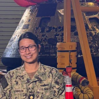 Georgetown graduate alum Kristi Johnson in front of the Artemis II Orion spacecraft. Johnson is wearing Navy fatigues.