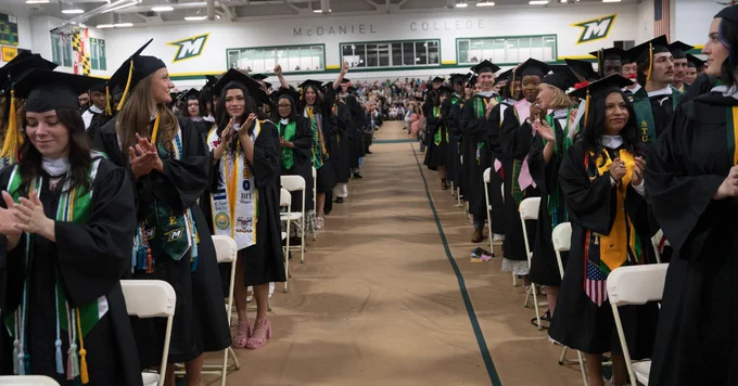 McDaniel College graduates in caps and gowns stand and clap in Gill Center during the Undergraduate Commencement Ceremony. 