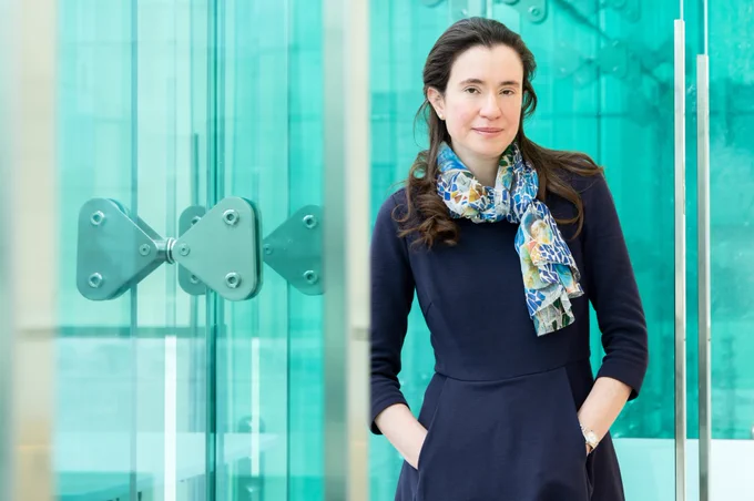Myriam Heiman stands along blue glass windows in MIT's Building 46