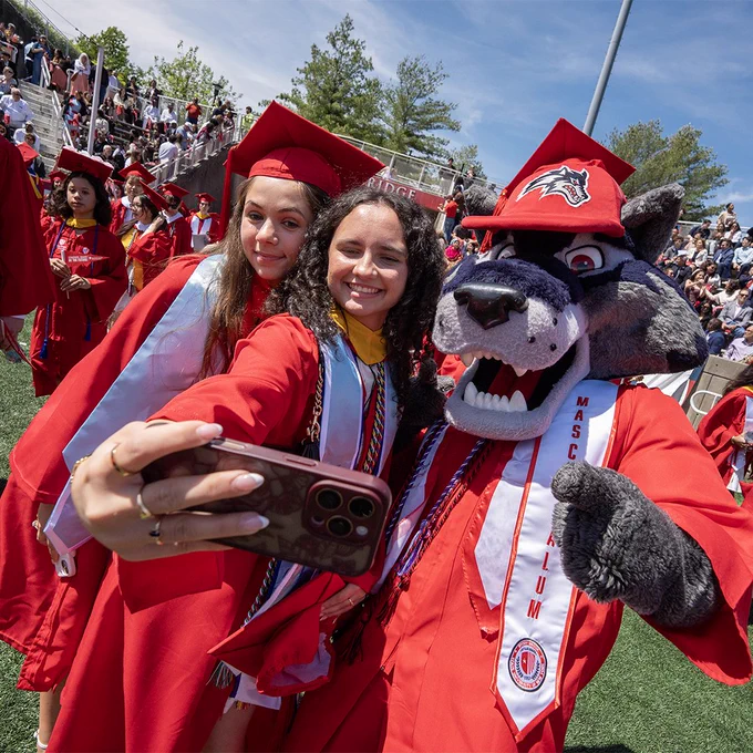 Graduates in red caps and gowns cheer and raise their hands during Stony Brook University’s commencement ceremony.