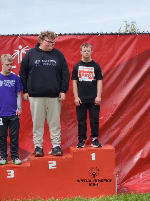Three young athletes stand on a Special Olympics Iowa podium with first, second, and third place positions against a red backdrop.