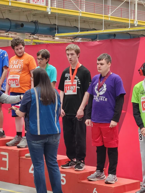 Three young athletes stand on a winners' podium with medals around their necks during an indoor sports event.