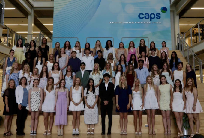 Large group of young people in formal attire posing in front of a blue backdrop with the text "CAPS" visible.