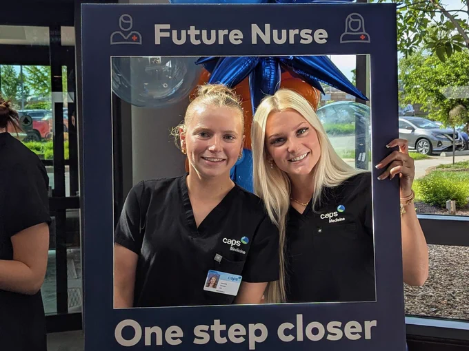 Two smiling women in black scrubs posing in front of a "Future Nurse One step closer" banner.