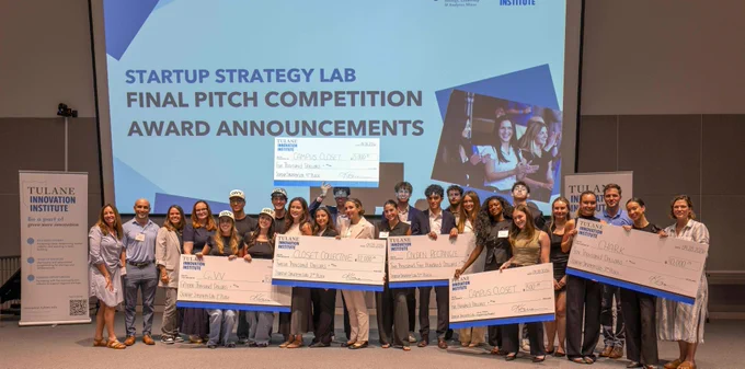 A group of Tulanians standing on stage holding large checks and smiling. The backdrop displays "Startup Strategy Lab Final Pitch Competition Award Announcements" from the Tulane Innovation Institute.