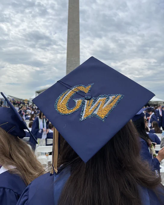 A graduate wearing a cap decorated with the George Washington University athletics logo.