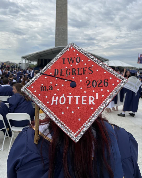 A graduate wearing a cap that reads “two degrees hotter. M.A. 2026.”