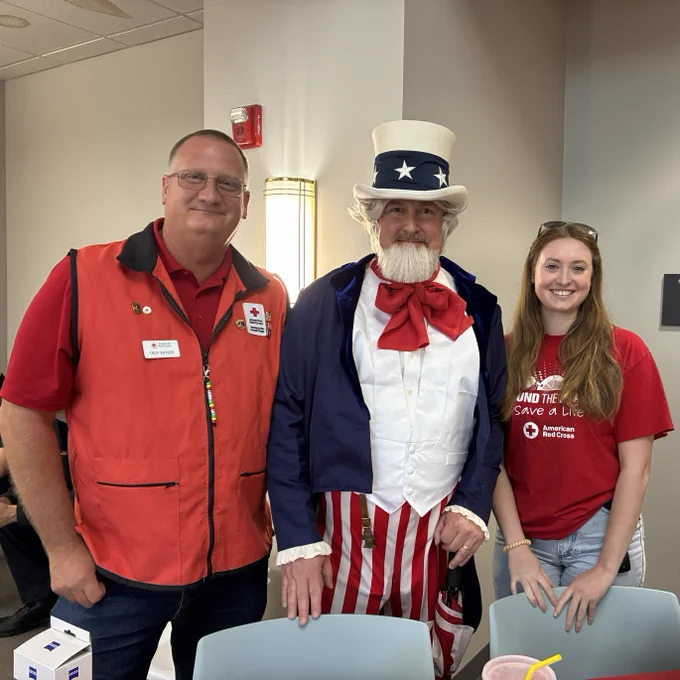 Two Red Cross volunteers stand on either side of a third person dressed as Uncle Sam.