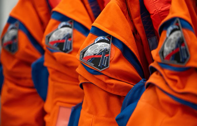 The Artemis II mission patch is seen on the right shoulder of four orange Orion Crew Survival System suits on Jan. 17, 2026, in the suit-up room of the Neil A. Armstrong Operations and Checkout Building at NASA’s Kennedy Space Center in Florida. The mission patch contains imagery of the Moon and the Earth. Credit: NASA/Joel Kowsky