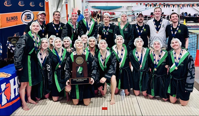 A high school water polo team poses proudly with their state third place trophy. The mood is celebratory as they wear medals and team robes.