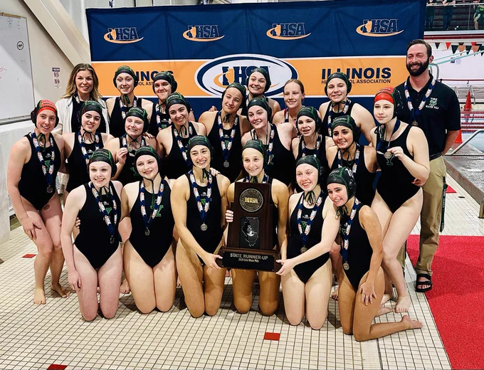 A joyful women's water polo team poses with their state runner-up trophy and medals. Smiling athletes project a sense of teamwork and achievement.