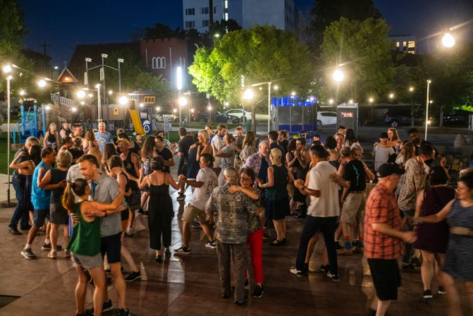 Large group of people dancing outdoors at night under string lights in a lively social gathering.