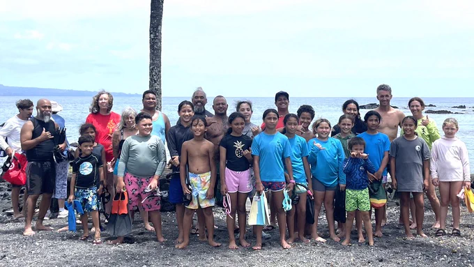 At the May 9, 2026, He Pūkoʻa Kani ʻĀina event, 5th graders from Ka ʻUmeke Kāʻeo, a charter and Hawaiian immersion school nearby in Keaukaha taught by Kaʻaka Swain, gather for a group photo at Puhi Bay. The past year, the students in Swain’s class have been learning how to monitor salinity, temperature, and coral reef ecology in preparation for the coral outplanting event. (Photo: Samantha Dane/UH Hilo Stories)