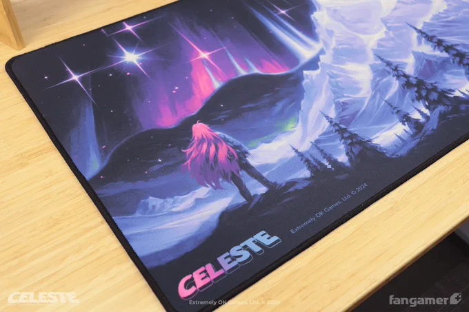 A photo of the Celestial Skies desk mat, part of our Celeste collection. This photo shows the bottom left part of the mat, with the Celeste logo at the bottom and Madeline staring out toward the mountaintop at night in a panoramic illustration. 