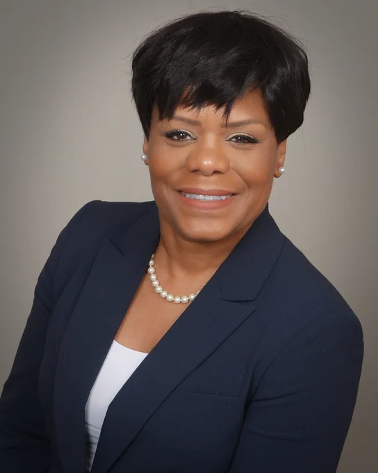 Head shot Dr. Cheryl Thaxton, smiling, wearing a black blazer with white undershirt. Gray background.