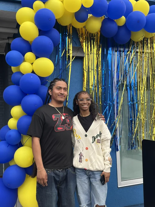 Two youth speakers smile and pose in front of a blue and yellow balloon arch at Casa Colibri.