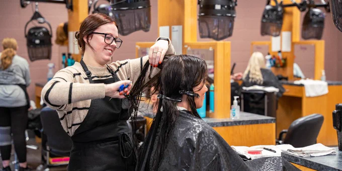 A person in a salon receiving a haircut from a stylist in a busy, well-equipped salon environment.
