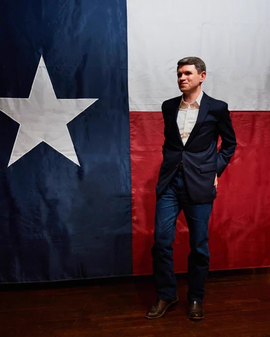 Democratic Texas U.S. Senate candidate James Talarico in a blue suit standing in front of a Texas flag. 