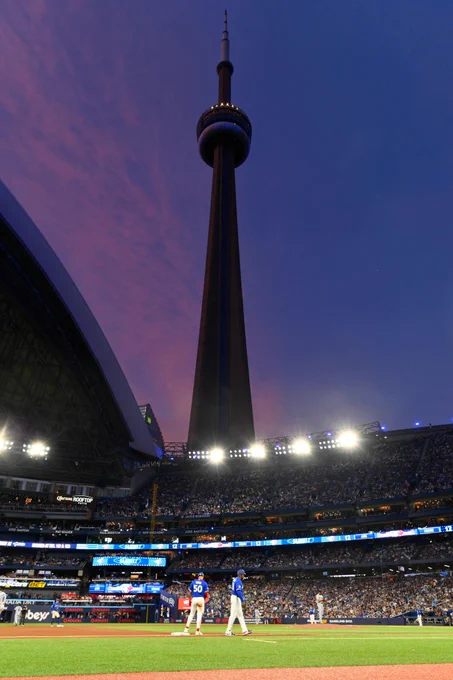 A low-angle shot of the CN Tower visible through the open roof at Rogers Centre in Toronto. A purple and blue sky can be seen behind the tower.
(Photo: Colton Hall/Major League Baseball)