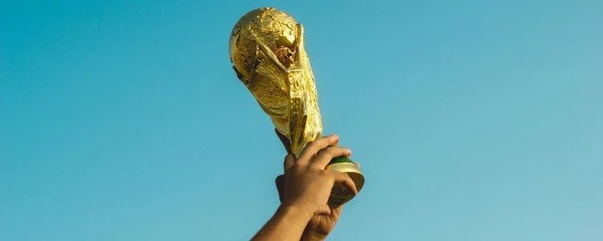 Hands holding up the World Cup trophy. Photo by Fauzan Saari on Unsplash. 