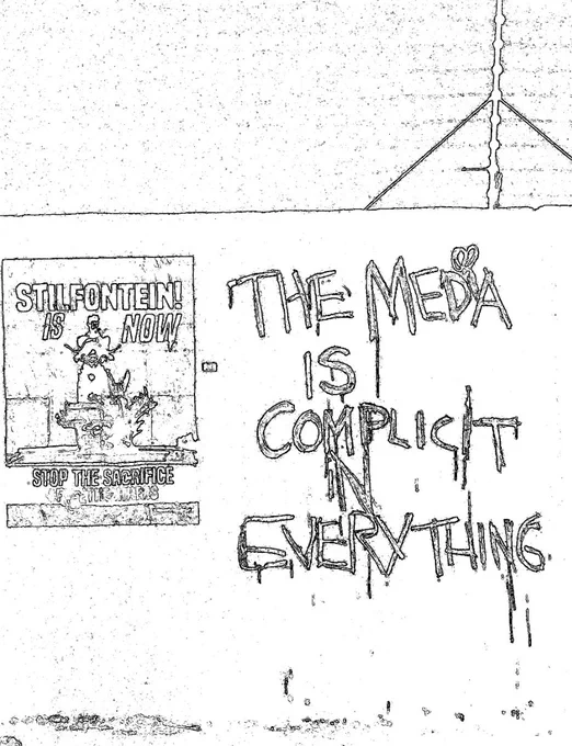 On a wall is text “The media is complicit in everything” and another poster that says “Stilfontein is now. Stop the sacrifice” with a few words below scratched/blurred out. There is a figure in the middle.