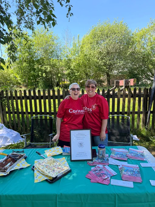Two people wearing matching red Caritas shirts standing behind a table with baked goods and informational pamphlets