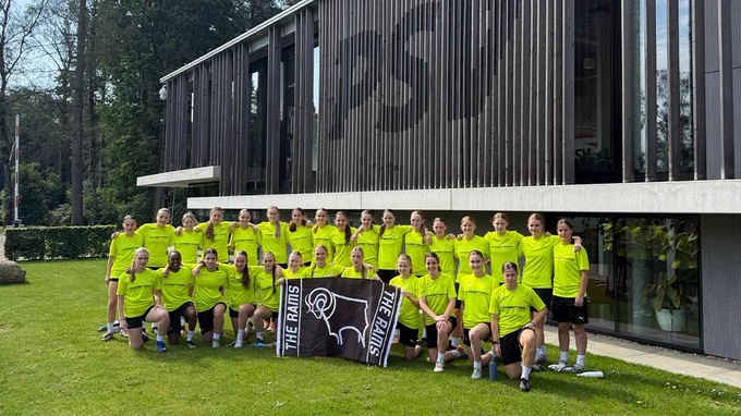 Derby County FTP U18 and U21s posing for a squad photo, holding a Derby County flag outside PSV Eindhoven's Training Complex - De Herdgang.