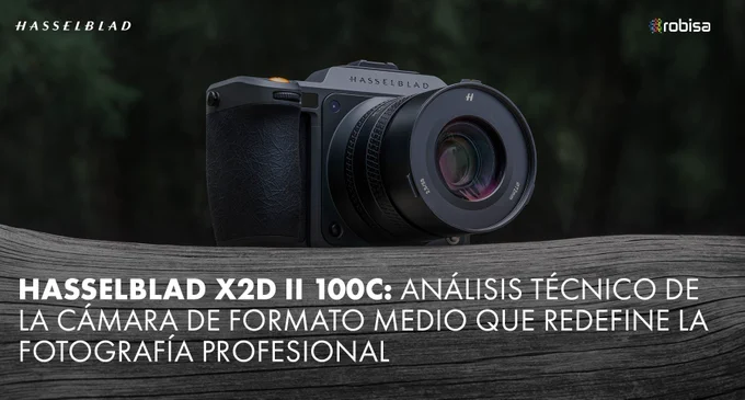 Hasselblad X2D II 100C con objetivo XCD sobre superficie de madera, fondo oscuro desenfocado. Cuerpo en aluminio anodizado gris oscuro con empuñadura de cuero negro y botón naranja de disparo. Logos Hasselblad y ROBISA en la imagen. Título del artículo superpuesto en la parte inferior.