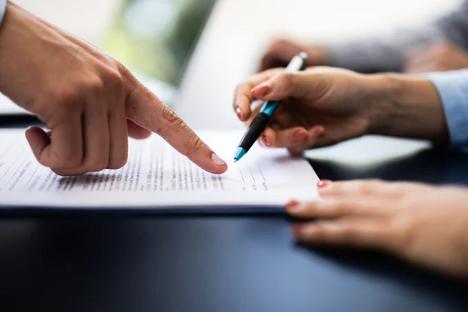 Close-up of two people reviewing and discussing a document with one pointing and the other holding a pen.