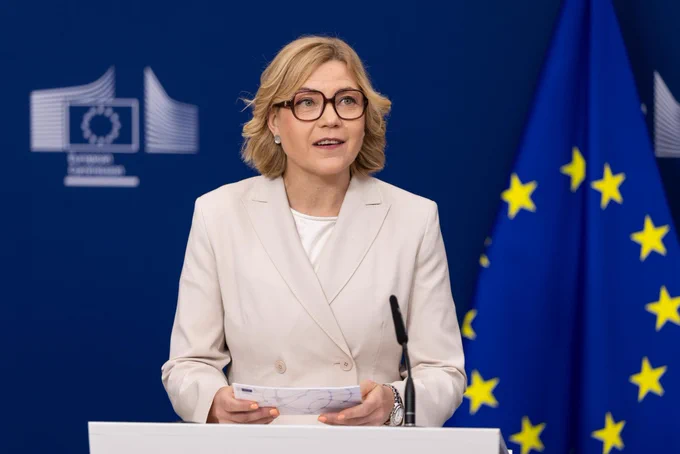 EVP Henna Virkkunen speaks at a European Commission press briefing podium, with EU flags and the European Commission logo in the background.