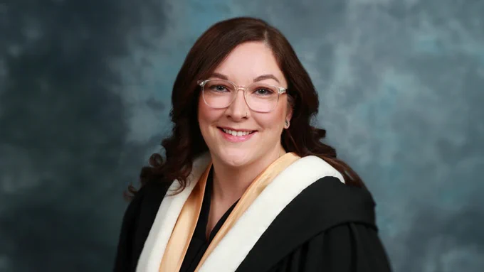 UNB graduate Meaghan Mead in her regalia on a blue background. 