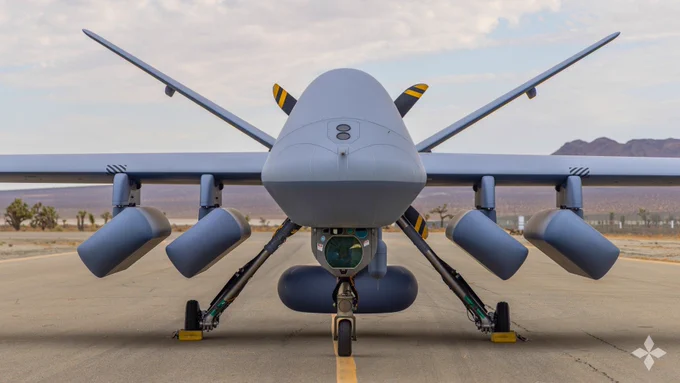 Front view MQ-9B SeaGuardian remotely piloted aircraft system equipped with multiple sonobuoy dispensing systems for anti-submarine warfare capability on a runway under a cloudy sky.