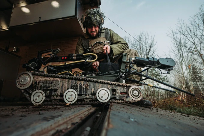 A soldier operating a tracked bomb disposal robot outdoors.
