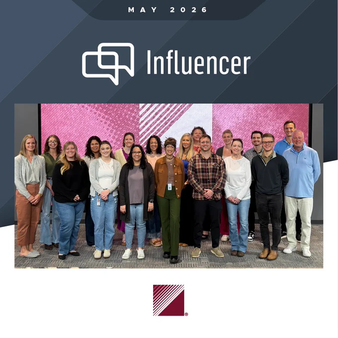 Group photo of 17 diverse professionals standing indoors against a pink and white patterned wall, taken in May 2026 for Crucial Influence. 