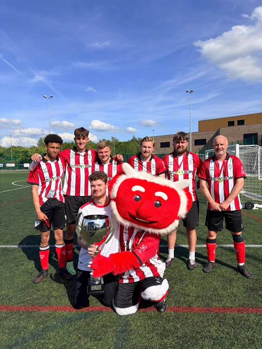 Several individuals stand together, smiling with a large, friendly mascot in a lively atmosphere.