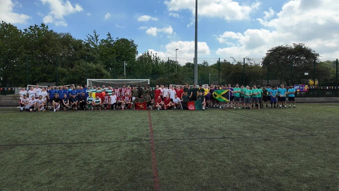  Several individuals stand together. They are football teams all lined up in a row.