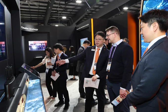 Group of professionals in business attire discussing and pointing at a digital display in a modern exhibition booth.