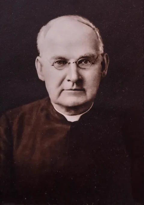 A vintage portrait of Brother Columba,
an individual wearing glasses and formal attire. The background is plain and dark.