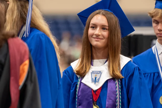 Young woman in blue graduation gown with tassel, smiling proudly at camera.
