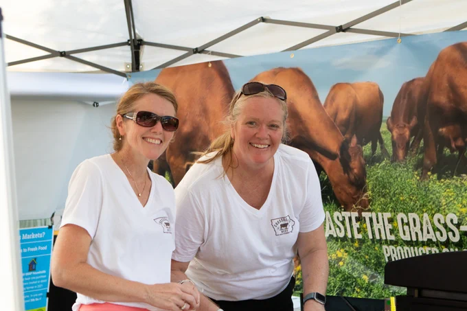 Two people posing for a photo as they cut sausage for samples at the Iowa State Fair Famers Market.