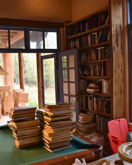 Stacks of books sit on a pool table inside a room at Cormac McCarthy’s home as boxes wait outside the open doors.