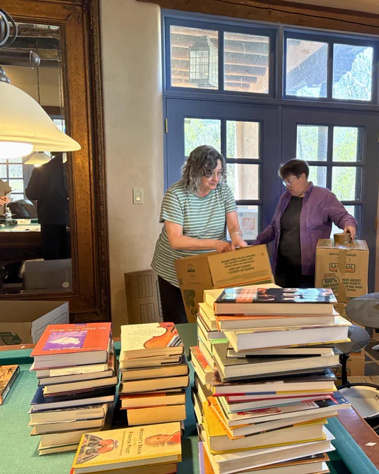 Two individuals sort and stack books from Cormac McCarthy’s personal library inside a room lined with bookshelves.