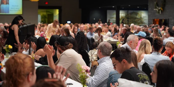A large gathering of people seated at round tables in a banquet hall.