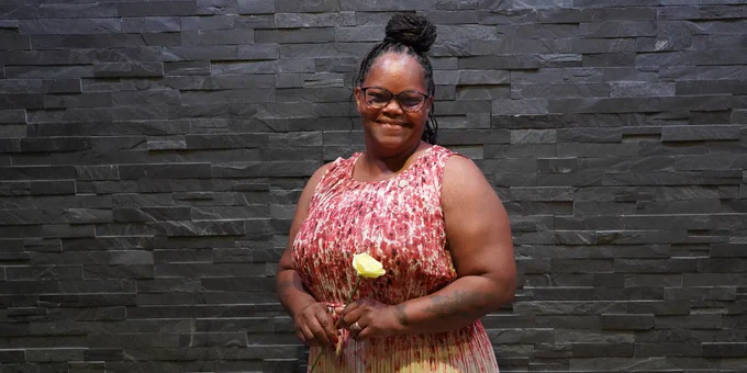 A person wearing a red and white patterned dress and holding a single yellow rose.