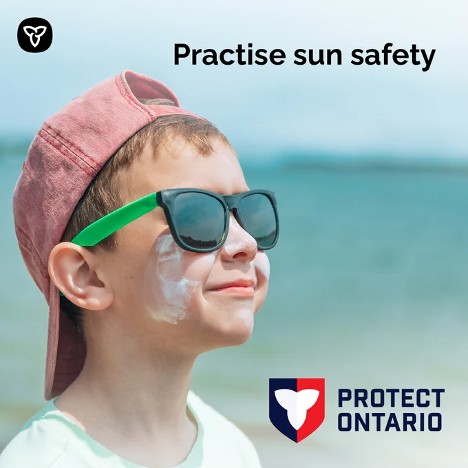 Child near a lake wearing a hat, sunglasses and sunscreen. Image Text: Practise sun safety.