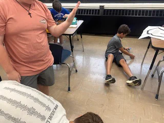 A student sits on the floor of the classroom, working with their robot. 